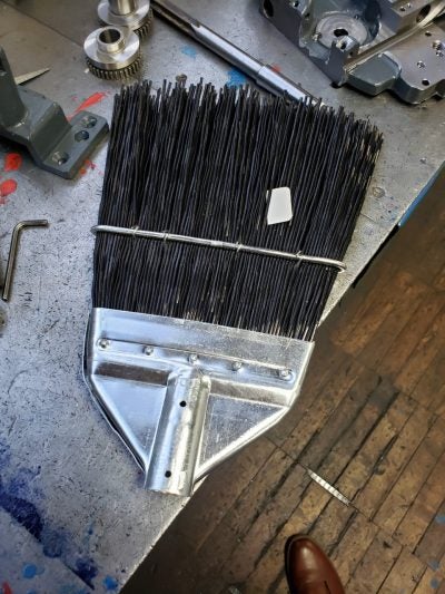 Industrial push broom head with metal plate on workshop table.
